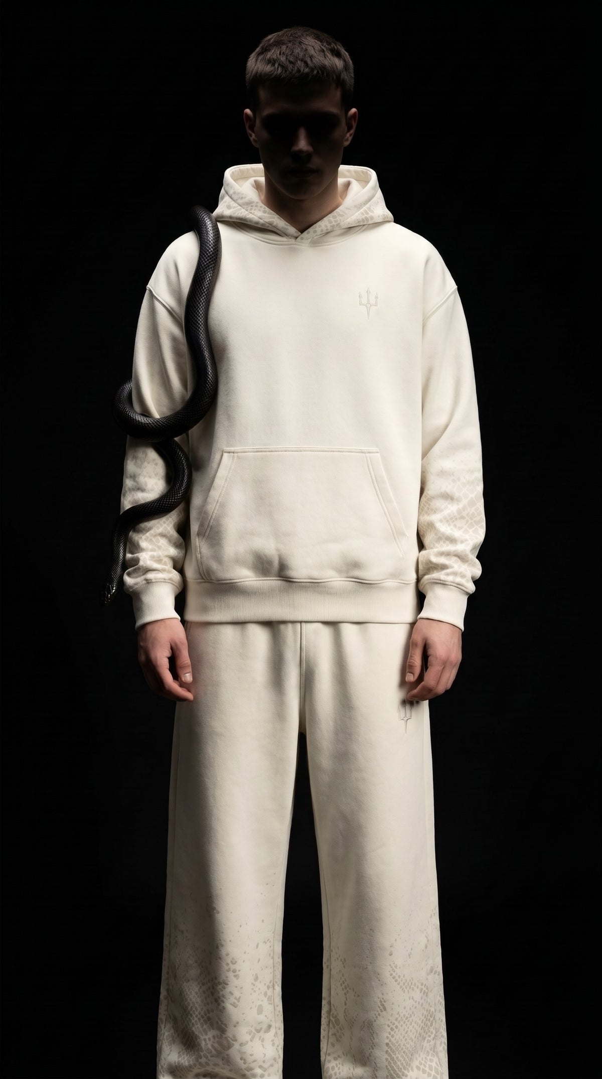 Conjunto Trinova completo en marfil: sudadera oversize con capucha y pantalón wide leg, sobre fondo negro, con una serpiente negra sobre el hombro